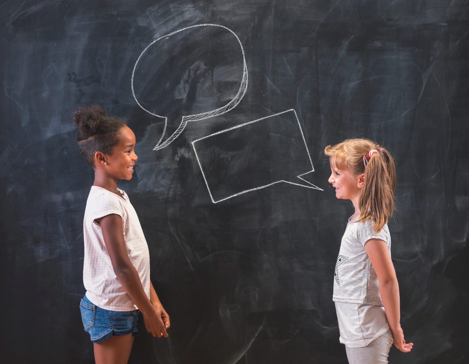 Two students talking in front of a chalkboard with speech bubbles drawn above them
